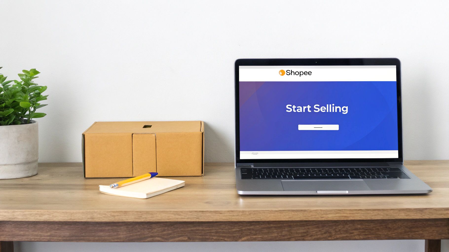 A laptop displaying Shopee’s ‘Start Selling’ page, a brown delivery box, and a plant on a wooden desk.